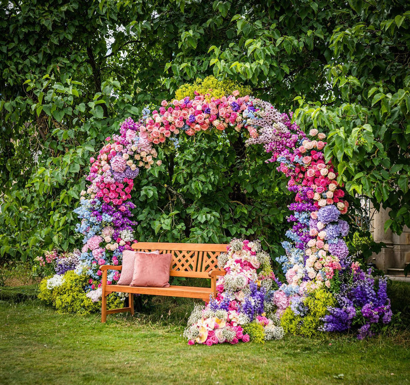 Colourful floral moongate surrounding a wooden bench at a London event by London Event Florist